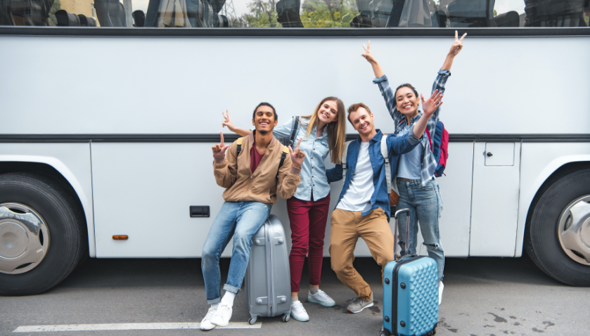 Cheerful multiethnic tourists with travel bags standing Infront of a coach bus