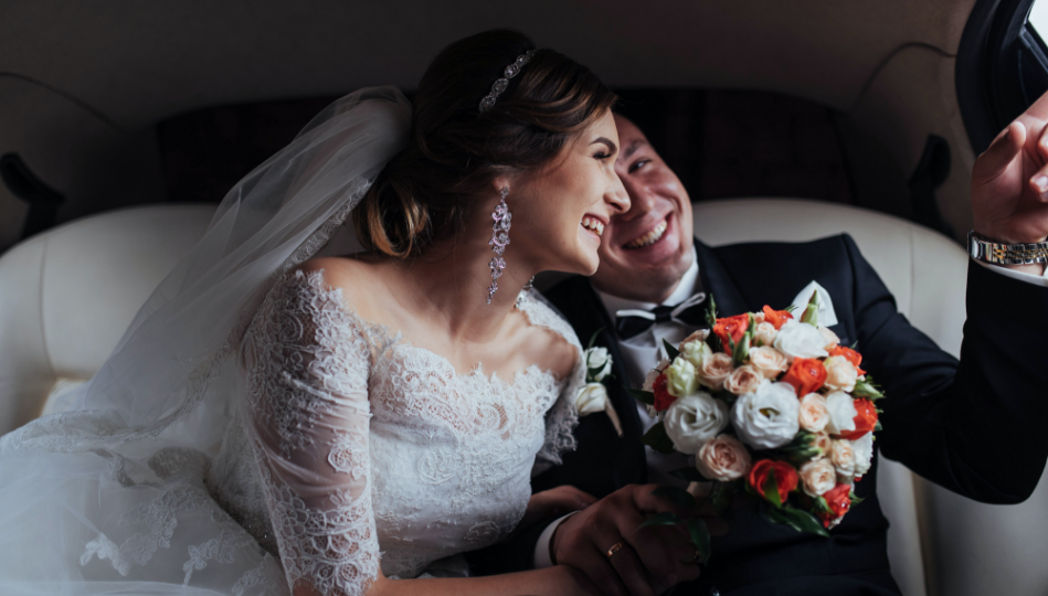 Happy man and woman in wedding dress smiling and pointing out of the car window