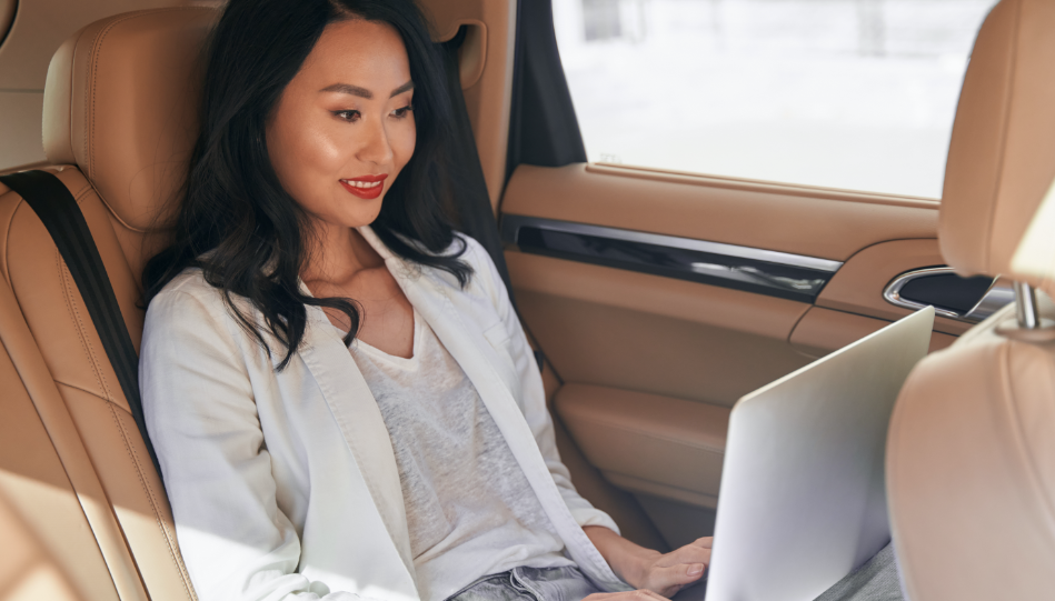Positive and confident business lady seating in a car smiling and looking at the laptop screen